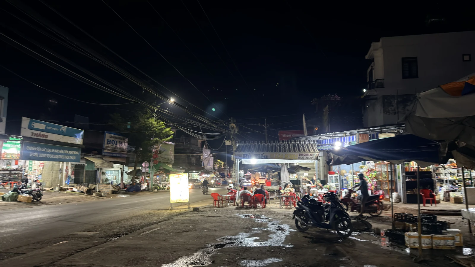 Cổng chợ Nam Ban buổi tối, vài sạp còn mở đèn và mấy bộ bàn ghế nhựa có người ngồi ăn trước cổng