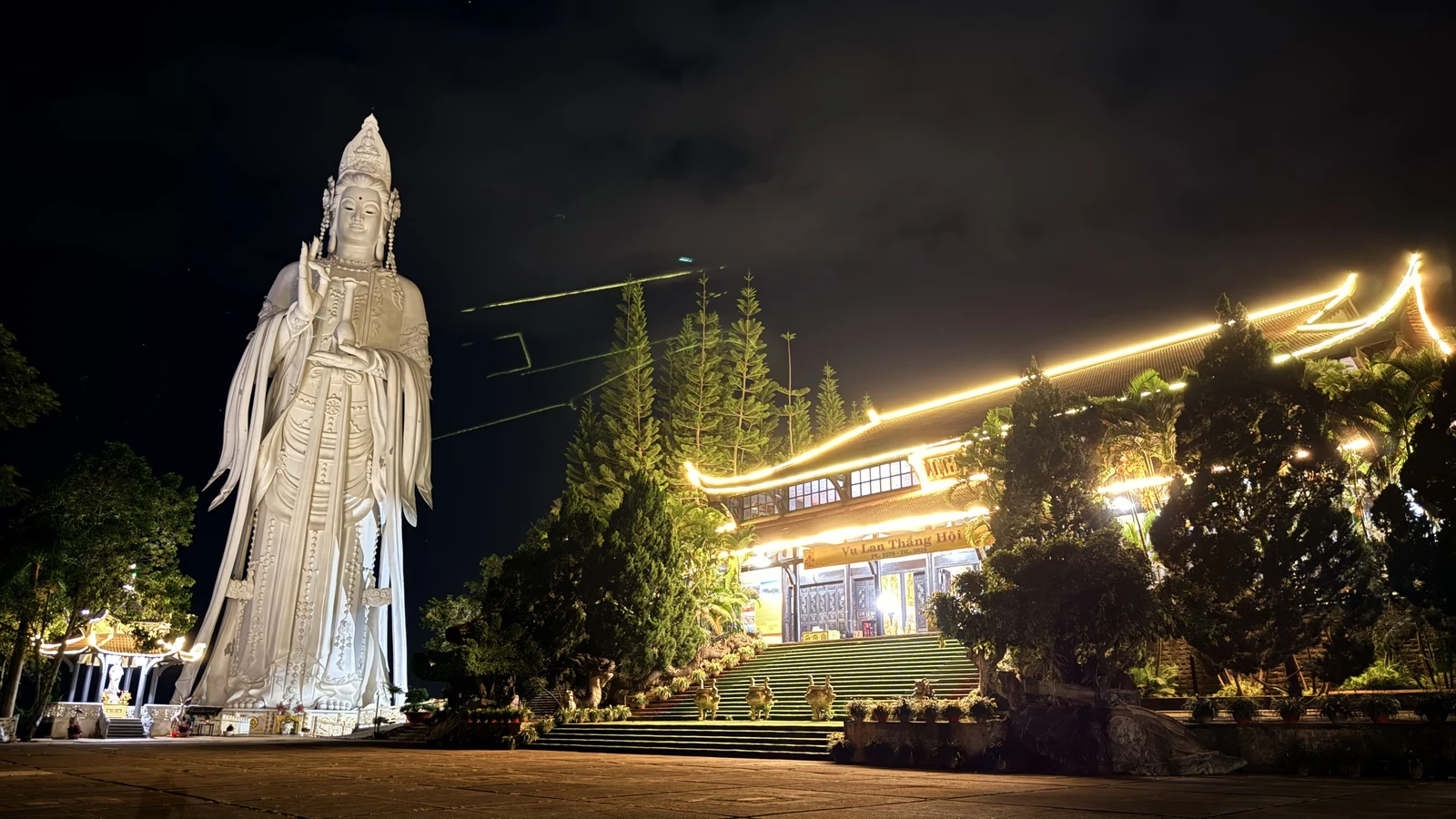 Tượng Quan Âm chùa Linh Ẩn và chánh điện lên đèn ban đêm, viền mái sáng vàng, bậc thang dẫn lên chùa