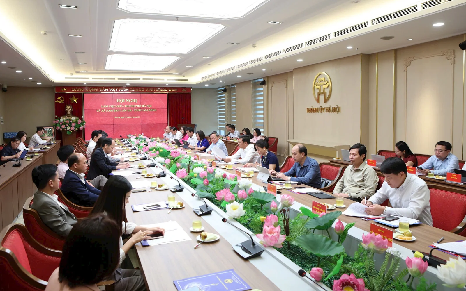 Toàn cảnh phòng họp Thành ủy Hà Nội nhìn dọc bàn dài, hai hàng đại biểu ngồi hai bên, cuối phòng là màn hình đỏ ghi tên hội nghị làm việc giữa thành phố Hà Nội và xã Nam Ban Lâm Hà