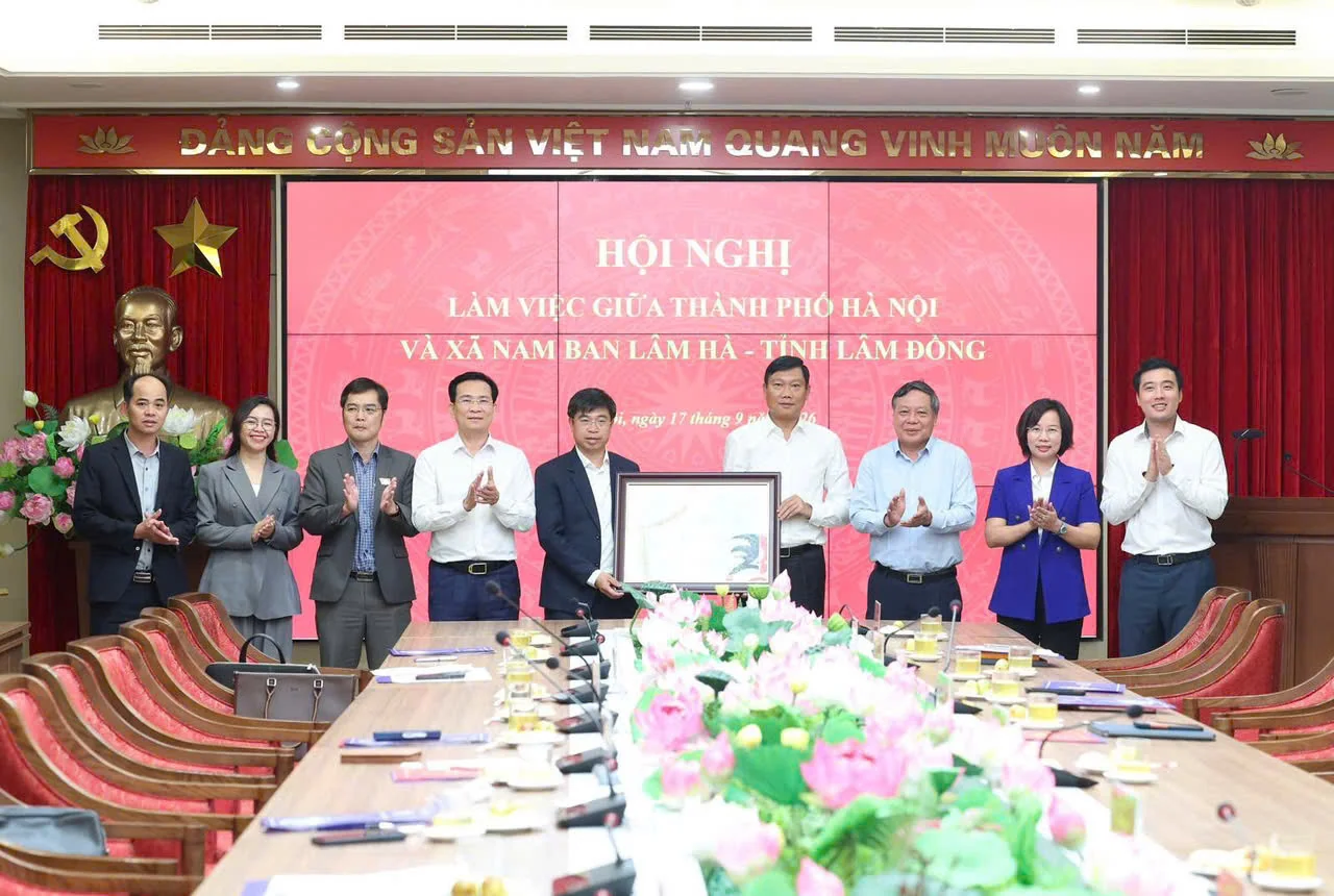 Hai đoàn đại biểu đứng thành hàng trước phông hội nghị ghi Làm việc giữa thành phố Hà Nội và xã Nam Ban Lâm Hà, tỉnh Lâm Đồng, Hà Nội ngày 17 tháng 9 năm 2026; ở giữa hai người cùng cầm một bức tranh có khung