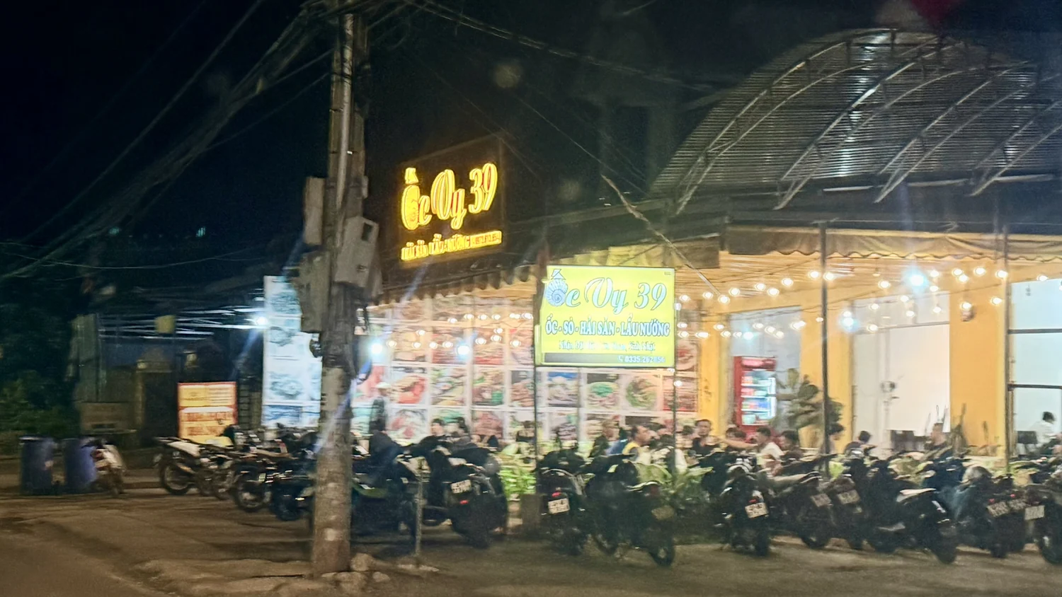 Quán Ốc Vy ở Nam Ban buổi tối, biển đèn sáng, xe máy đậu kín trước quán, khách ngồi bên trong