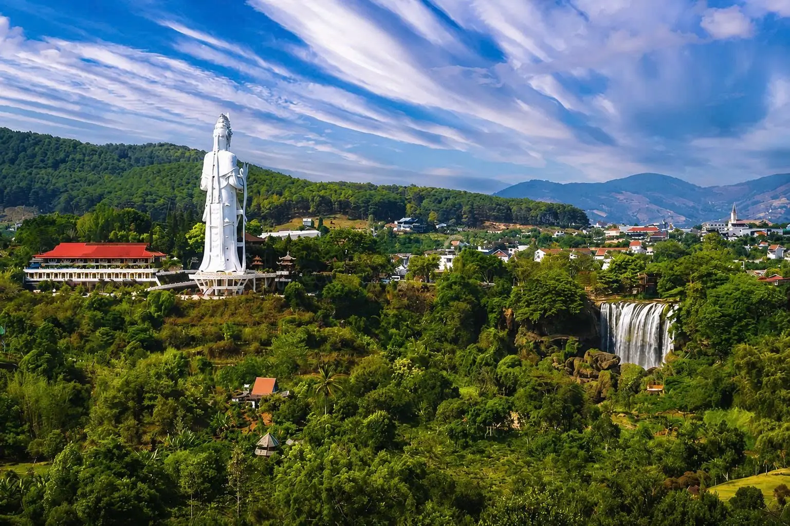 Toàn cảnh trung tâm Nam Ban: tượng Quan Âm chùa Linh Ẩn, thác Voi và nhà dân trên đồi, núi phía sau